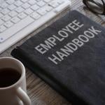 An employee handbook and a cup of coffee in front a work computer keyboard.