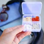 A box of pills with a travel bag in the background.