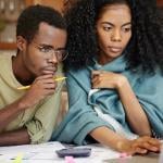 Young Black couple looking over laptop screen with papers and a calculator sitting on the table