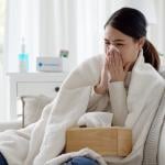 Young woman with a cold sitting under a blanket on a sofa.