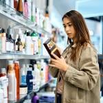 Young woman reading the label of a skincare product in a shopping mall.