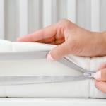 A woman's hand opening the cover of new white mattress to check the quality of a baby's bed.