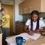 Two young adult women who are roommates in a small apartment.