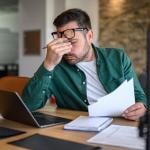 Anxious landlord rubbing eyes while looking at documents.