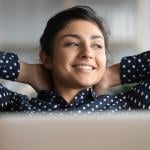 Satisfied woman happily sitting  at work with her hands behind her head.