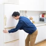 Man fixing the placement of his fridge in the kitchen.