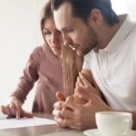 Two people looking over paperwork carefully, lit by window light during the daytime. 