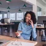 Businesswoman in her workplace looking at her credit card while on the phone.