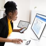 Woman using a phone and computer to use online banking.
