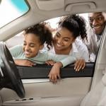 A family looking at the interior of a new car through its window.