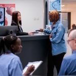 Patients and staff in a hospital reception desk area.