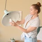 Young woman screwing light bulb into a ceiling lamp.