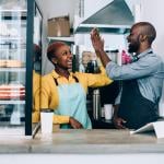 Cheerful black business owners giving high five to each other behind their store counter.