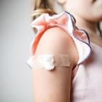 Close up of child's upper arm with a cotton ball and tape covering vaccination site. 