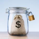 Concept of an emergency fund - a mini bag with a dollar symbol on it locked inside a jar.