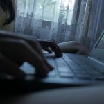 Silhouette of a person typing on a laptop at home.