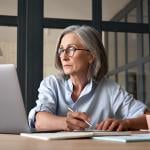 Senior woman looking up information online and writing notes.