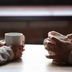 A Gen Z and Millenial sitting across each other at a table drinking coffee.