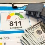 Figure of a house made of paper with credit report letters and cash around it.