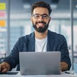 Worker in a modern office smiling while using a laptop.