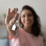 A young female homeowner holding up the keys to her house.