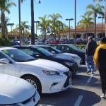 A parent and his teenagers looking at a row of used cars.