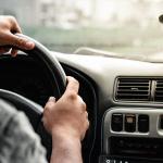 Close-up of a man holding the steering wheel while driving on the road.