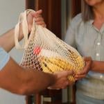  Man hands a net bag of groceries to woman in the doorway, their faces are not visible.