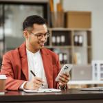 Small business owner holding a phone on his one hand and writing down information with the other.