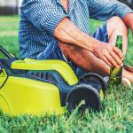 Senior man enjoying a bottle of beer beside a mower in his lawn.