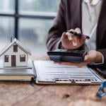 Property agent calculating taxes with a figure of a house and contract on a table.