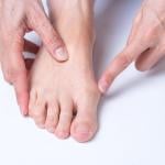 Top down view of light skinned person pointing to the bunion on their right foot.