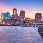 Cityscape image of Des Moines skyline, Iowa bridge over water with summer sunset.