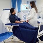 Patient sits getting hooked up to dialysis machine with nurse helping set up.
