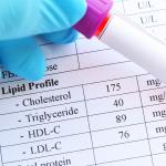 A blood sample in a test tube tube held in front of a printout of lipid profile test results. 