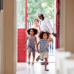 Two cute children with natural hair running into open door of house with grandparents in the background. 