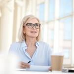 Blond professional sitting at table with large windows in the background talking in meeting.