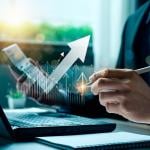 Person wearing a suit working on laptop and calculator, holding a pen with finance icons overlaid to symbolize money management.