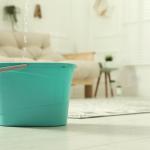 Close up of turquoise-colored plastic bucket on floor in living room with water dripping from ceiling into it.