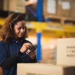 Warehouse worker using bar code scanner on boxed goods inside warehouse.