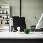 A modern empty office with a vacant chair behind a desk with a computer monitor and desktop decor.