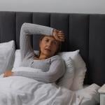 A middle-aged woman experiencing headache while sitting on bed.