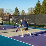 Two teams playing at a public park's pickleball court where a male player returns a volley at the net.