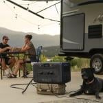 Couple at a table with a dog camping next to an RV.