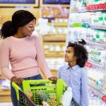 A young black mom and her daughter shopping together for groceries in a supermarket.