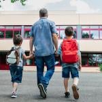 A father holding his two young boys and dropping them back to school.