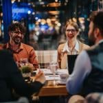 A group of business people laughing and discussing during a meeting in a modern restaurant setting. 
