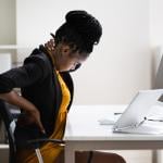 A female employee sitting in her office experiencing back pains.