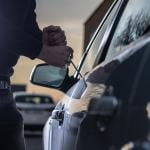 A thief trying to break into a car window with a screwdriver.