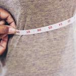 A tailor taking measurements of a client's torso with a tape measure.